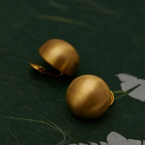 Macro detail of golden brushed metal half-ball stud earrings on textured green floral paper