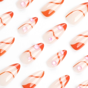 Short almond press-on nails with orange wavy lines and 3D pink rhinestones on white