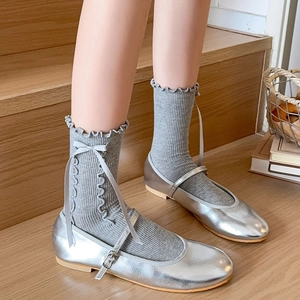Close-up of light grey socks with ruffled edges and bow details worn with silver shoes