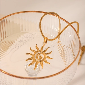 Close-up of golden sun pendant on a snake chain draped over a glass bowl