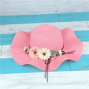 Close-up of pink straw hat with wide wavy brim and decorative daisy flowers on wood board