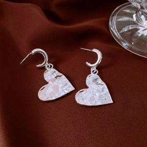 Detailed view of silver heart earrings with irregular lava texture on dark satin
