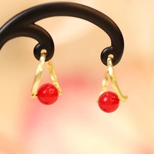 Macro shot of elegant gold earrings with vibrant round red beads on a black stand