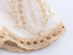 Detailed close-up of khaki geometric embroidery and scalloped hollow lace on white cotton fabric