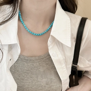 Close-up of minimalist turquoise beaded necklace worn with a white shirt