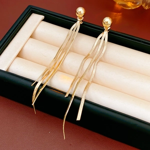 Detail von goldenen Quastenohrringen mit Kugelsteckern auf einem beigen Kissen