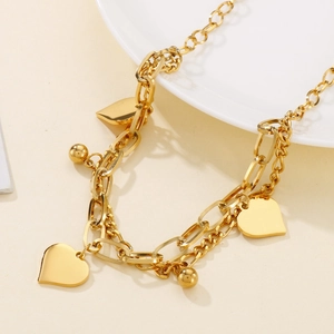 Detail of a double-layered gold heart bracelet and beaded chain on a white plate
