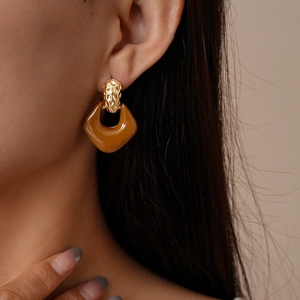 Detailed close-up of retro caramel resin and hammered gold metal earrings on model