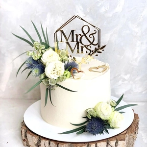 Detail of golden Mr & Mrs acrylic topper on a white floral wedding cake with wood base