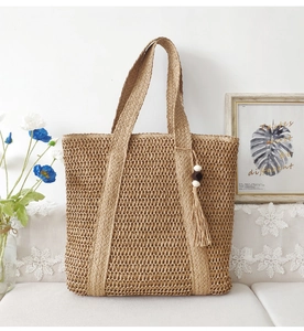 Close-up of high-quality woven straw texture and tassel charm on a beige tote bag