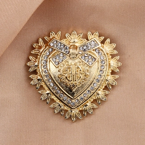 Macro detail of golden heart brooch with rhinestones and bow on beige silk fabric