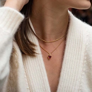 Detail shot of a layered gold necklace featuring a sparkling red heart topaz pendant