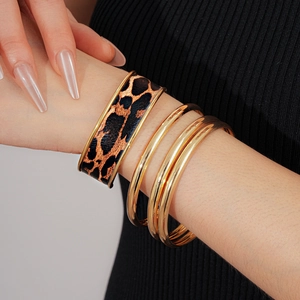 Détail de bracelets dorés superposés et d'un bracelet en cuir léopard sur un mannequin
