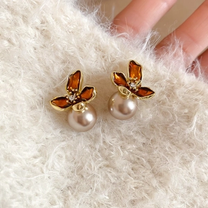 Detail of flower pearl earrings with orange enamel and zircon on a knit sweater