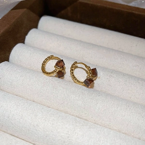 Detailed macro view of gold-plated twisted hoop earrings with amber square crystals