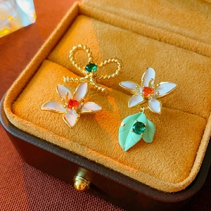 Macro shot of asymmetrical floral bow earrings with white enamel and orange gems