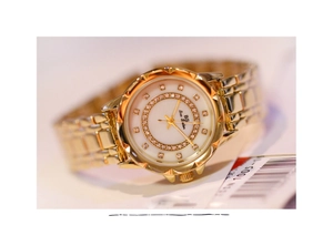 Detail of Bee Sister gold watch featuring a white mother-of-pearl dial and crystal bezel