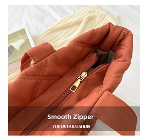Detailed close-up of smooth gold zipper and quilted diamond pattern on rust orange tote bag