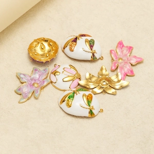 Gold plated stainless steel enamel flower and dragonfly pendants scattered on beige surface
