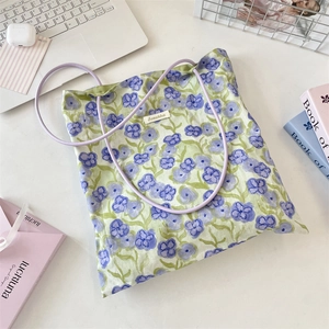 Dettaglio della borsa tote in tela floreale con manici viola e etichetta Sozakka su tavolo