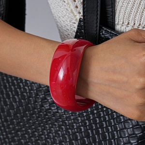 Close-up of a wide red acrylic geometric bangle on a wrist with high-gloss mirror finish