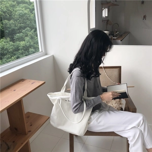 Detalle de un bolso tote de lona blanca minimalista con letras negras y textura de tela