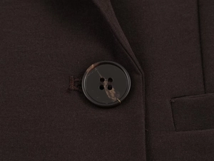 Gros plan du bouton à motif marbré et du tissu sergé sur le blazer marron foncé