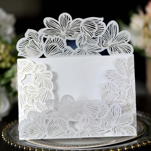 Macro shot of white laser-cut floral wedding invitation on elegant silver plate with flowers