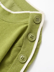 Detail of green knit sweater showing decorative shoulder buttons and white stripe trim