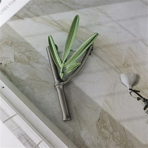 Bamboo style green leaf brooch with silver metallic branches on marble surface