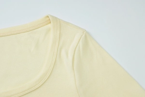 Close-up of crew neckline and double-needle stitching on light yellow knitted cardigan