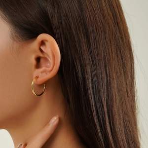 Close-up of golden hoop earring worn by a model showcasing polished steel texture