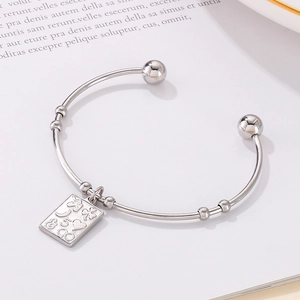 Detailed view of silver stainless steel open bangle with engraved rectangular charm on book