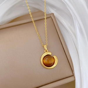 Close-up of golden necklace with a round amber cat-eye stone pendant on beige jewelry box