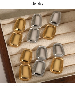 Detailed view of polished gold and silver rectangular pendant earrings on velvet display
