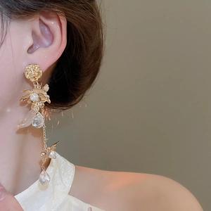Close-up of elegant gold flower earrings with pearl tassels on a model for a luxury look