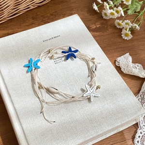 Detail of woven rope necklace with starfish, natural shells and gold beads on a book