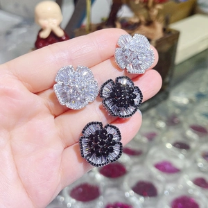 Close-up of camellia earrings with white and black zircons held by a hand