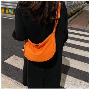 Close-up of bright orange nylon dumpling bag with adjustable strap on street background