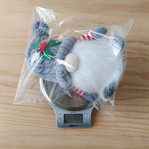 Detailed view of grey knitted Christmas gnome on scale weighing 100.1g for holiday decor