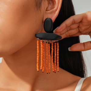 Close-up of bohemian tassel earrings with orange beads and black geometric wood studs