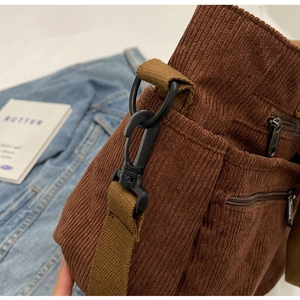 Detailed close-up of brown corduroy bag fabric with durable black metal hook and strap