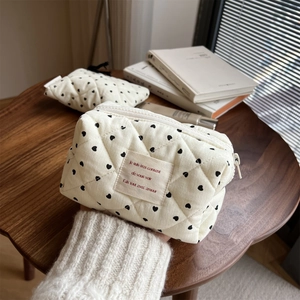 Macro view of cream quilted corduroy makeup bag with black hearts and woven label