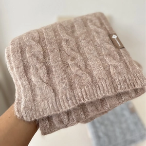 Close-up of brown knit scarf featuring classic cable pattern and textured brand logo tag