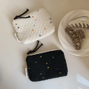 Dettaglio di portamonete in tweed bianco e nero con pois colorati e zip intrecciata