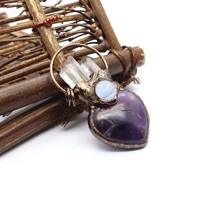 Detailed view of heart-shaped amethyst pendant with blue crystal on a rustic branch