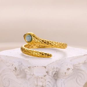 Detail of golden snake ring with blue gemstone on white classical stone pedestal