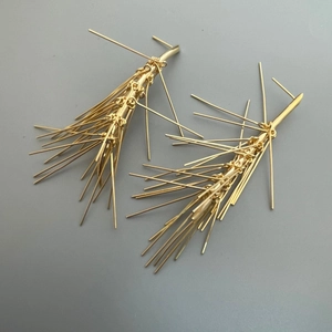 Dettaglio macro degli orecchini a ago di pino dorati con design radiale e moderno