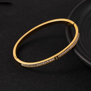 Elegante bracciale rigido in acciaio al titanio dorato con cristalli su sfondo nero