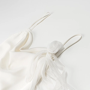 Detail of white satin dress featuring a 3D floral accent and delicate spaghetti straps